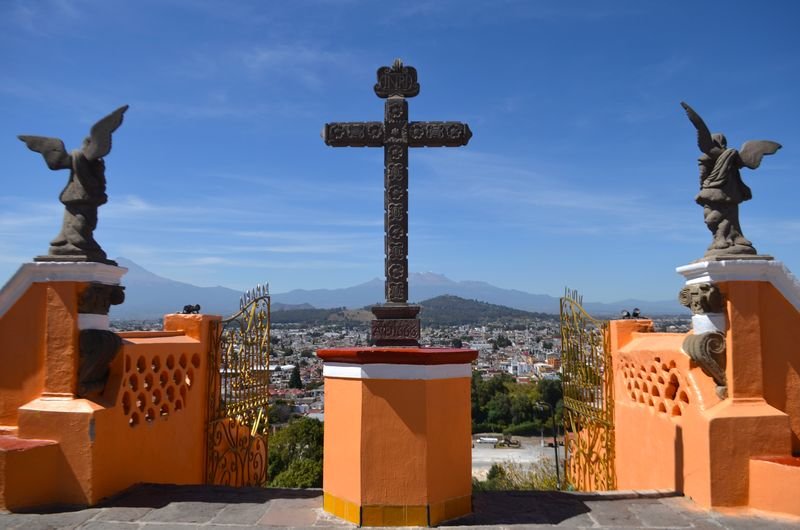 Cruz y ángeles en lo alto de Cholula, con los volcanes al fondo